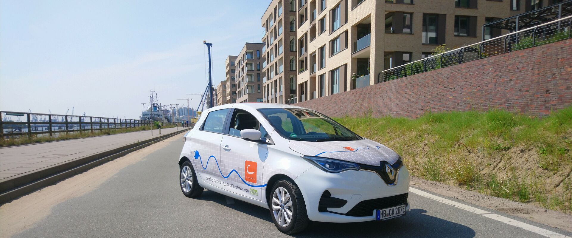 Ein E-Auto steht leicht schräg vor dem Panorama der HafenCity in Hamburg