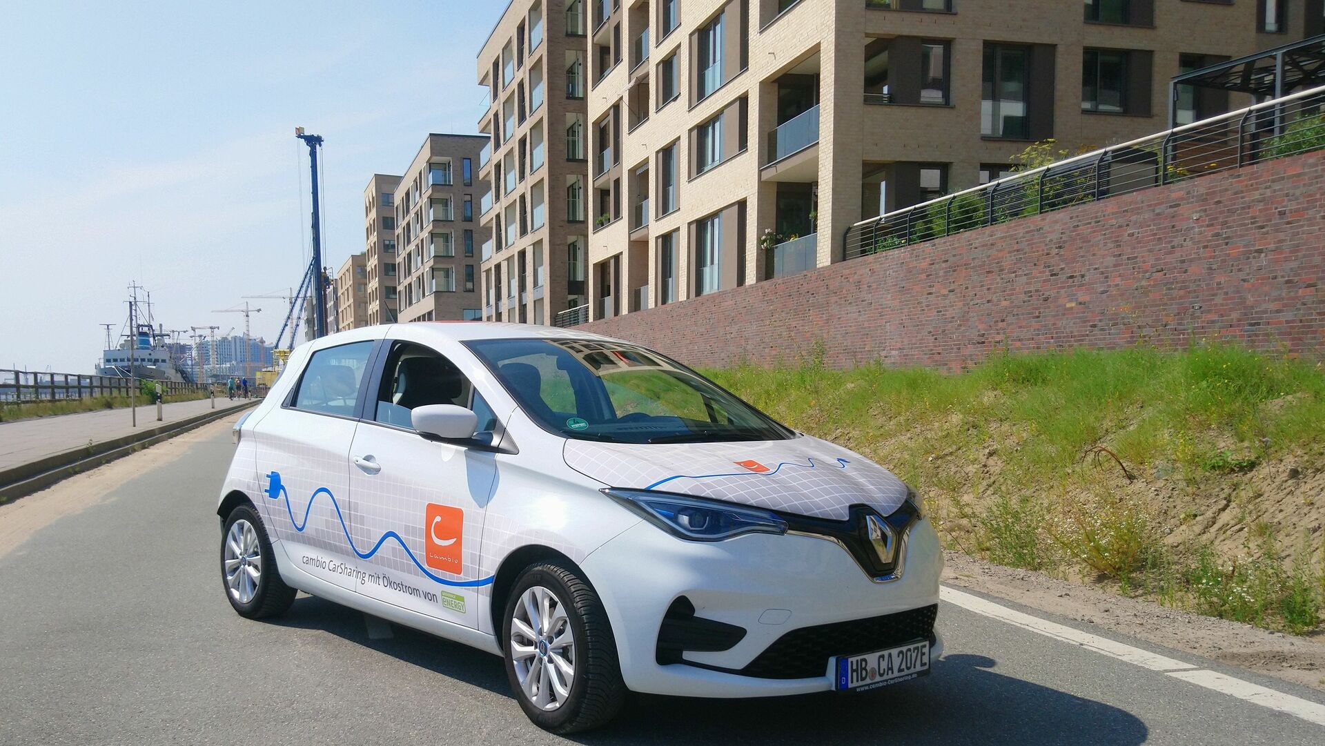 Ein E-Auto steht leicht schräg vor dem Panorama der HafenCity in Hamburg