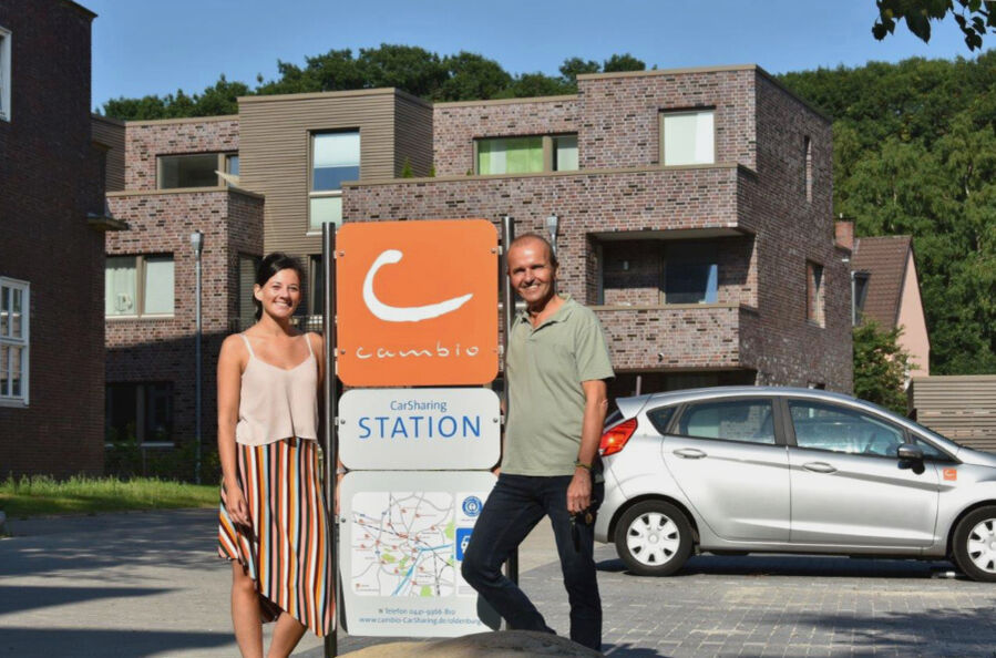 Ein Mann und eine Frau stehen an einer cambio-Station. Im Hintergrund: Ein cambio-Auto.