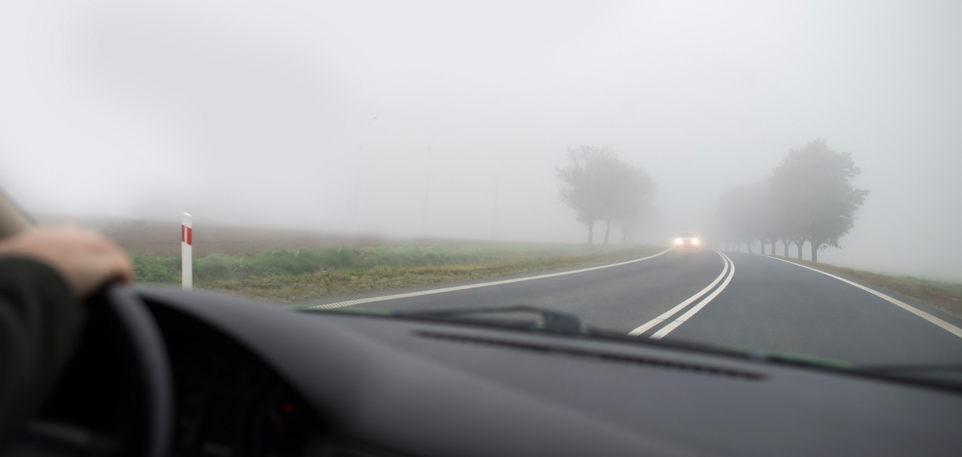 Ein Auto fährt im Nebel eine Straße entlang.