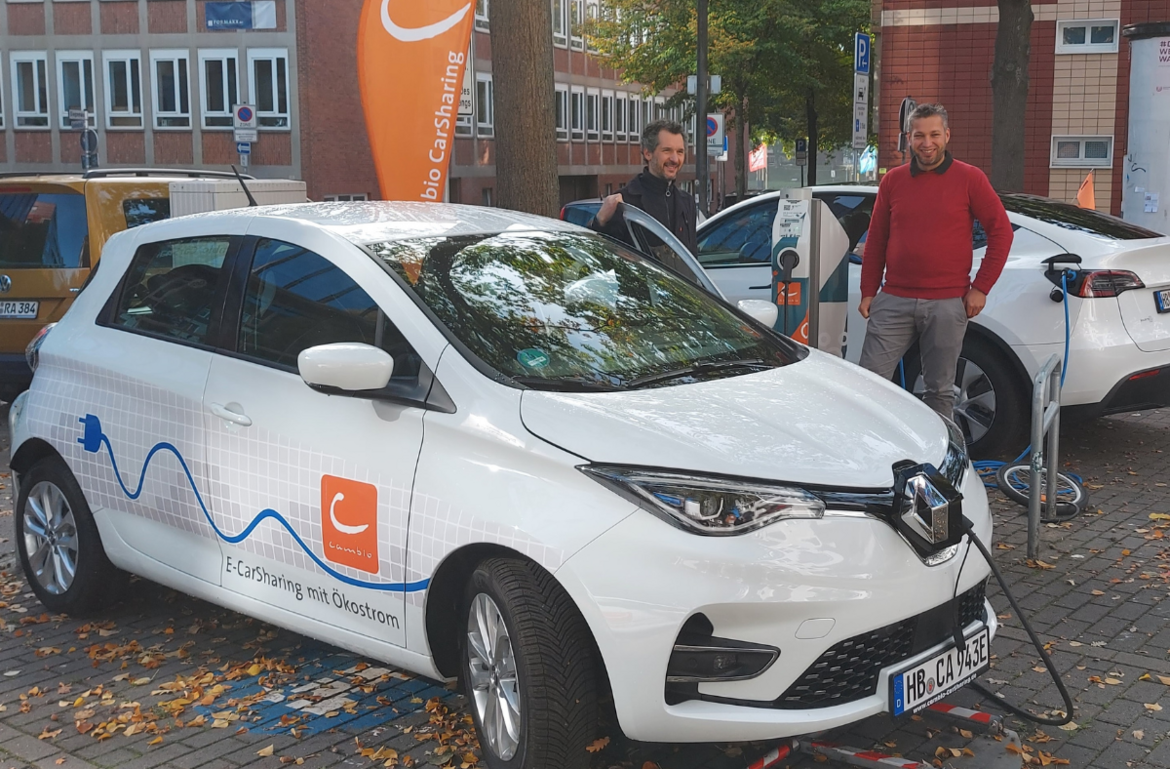 Ein cambio-Auto parkt in Bremen vor einer Ladesäule. Mit auf dem Bild zwei Männer.