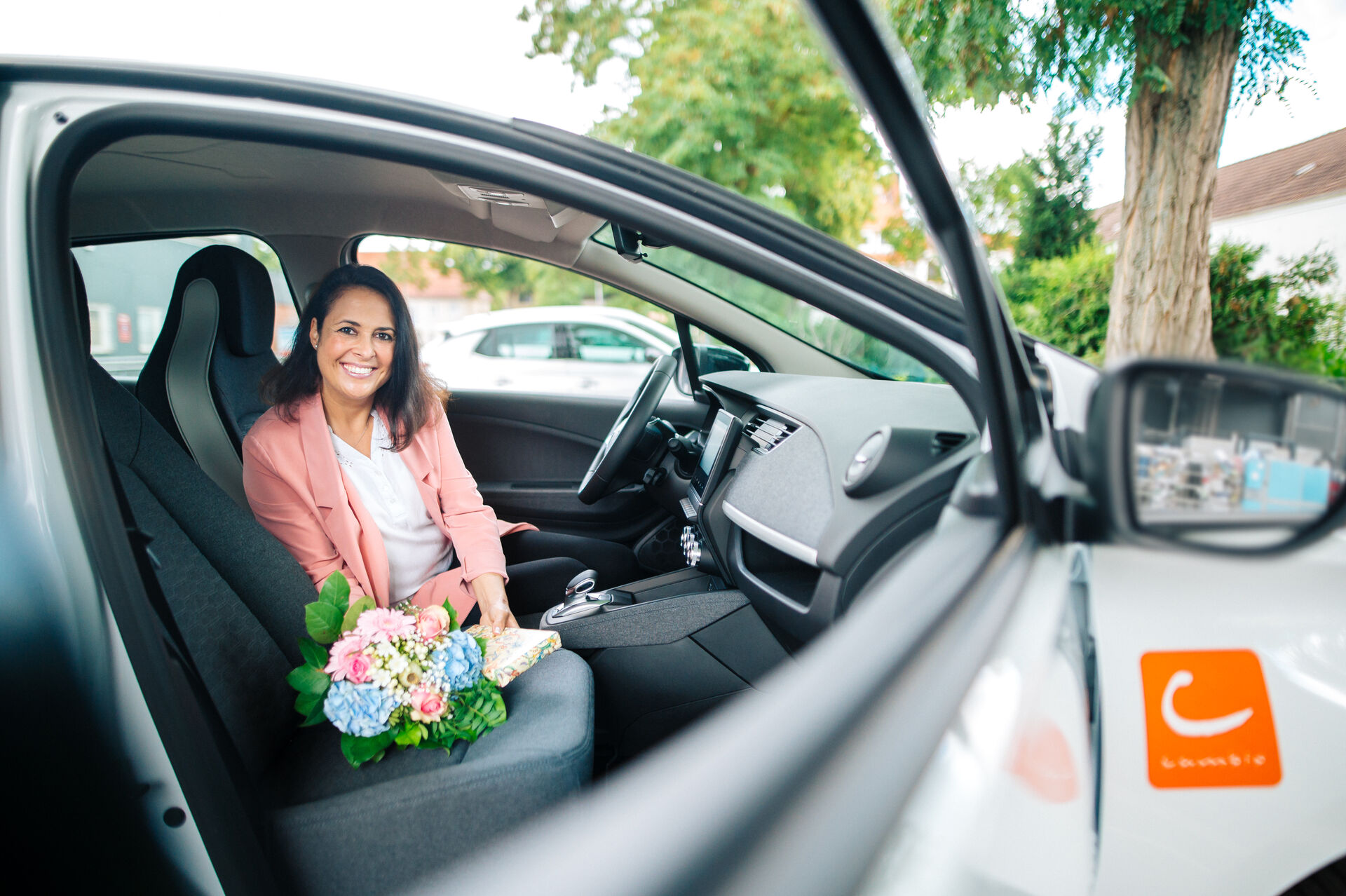 Frau sitzt am Steuer eines cambio-Autos. Auf dem Beifahrersitz liegt ein Blumenstrauß.