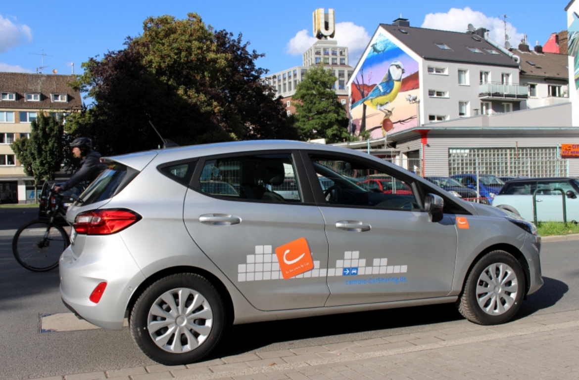 cambio-Auto parkt vor bemalter Hauswand. Im Hintergrund das Dortmunder U.