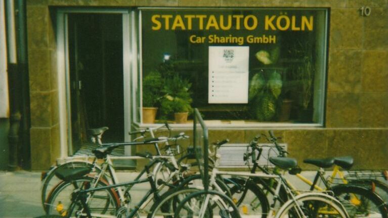 Geschäftsstelle Stattauto, man sieht ein großes Fenster mit dieser Aufschrift. Davor ein Fahrradständer mit mehreren Rädern.