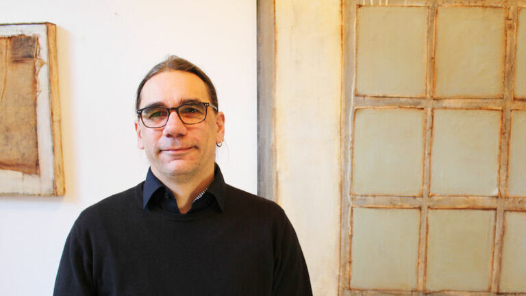 Mann mit Brille und schwarzem Pullover steht vor Leinwand