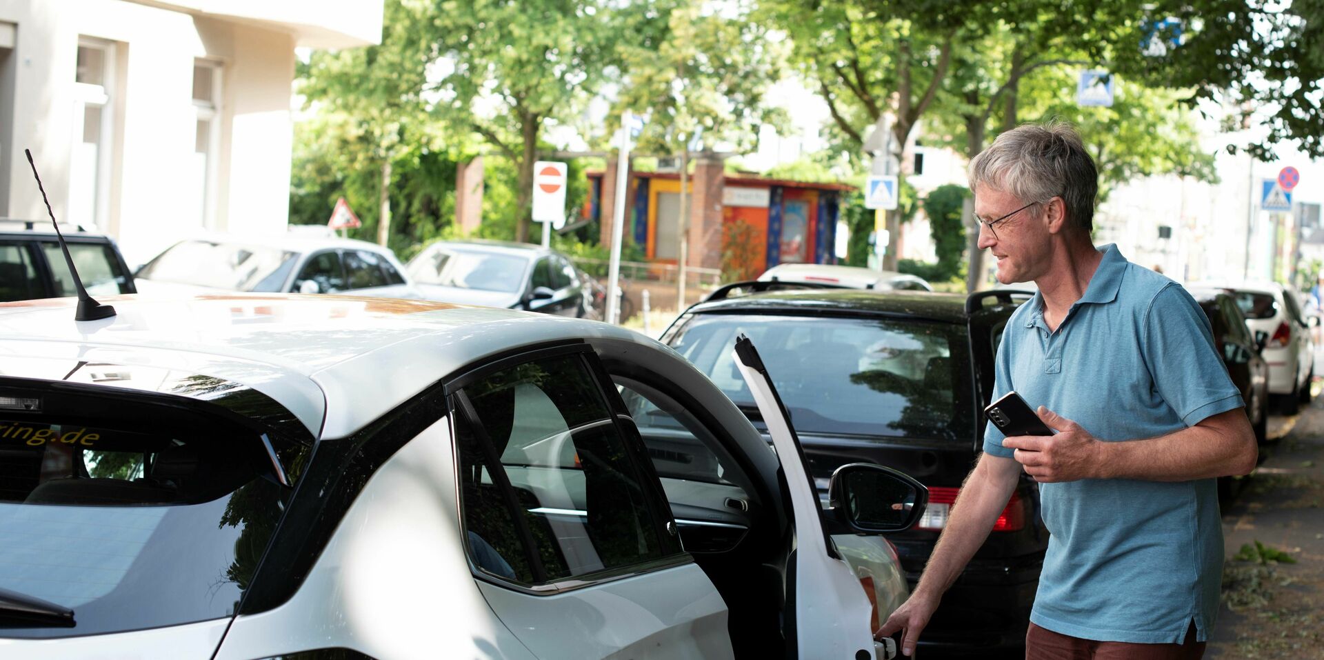 Ein Mann öffnet die Beifahrertüre eines am Straßenrand parkenden CarSharing-Autos