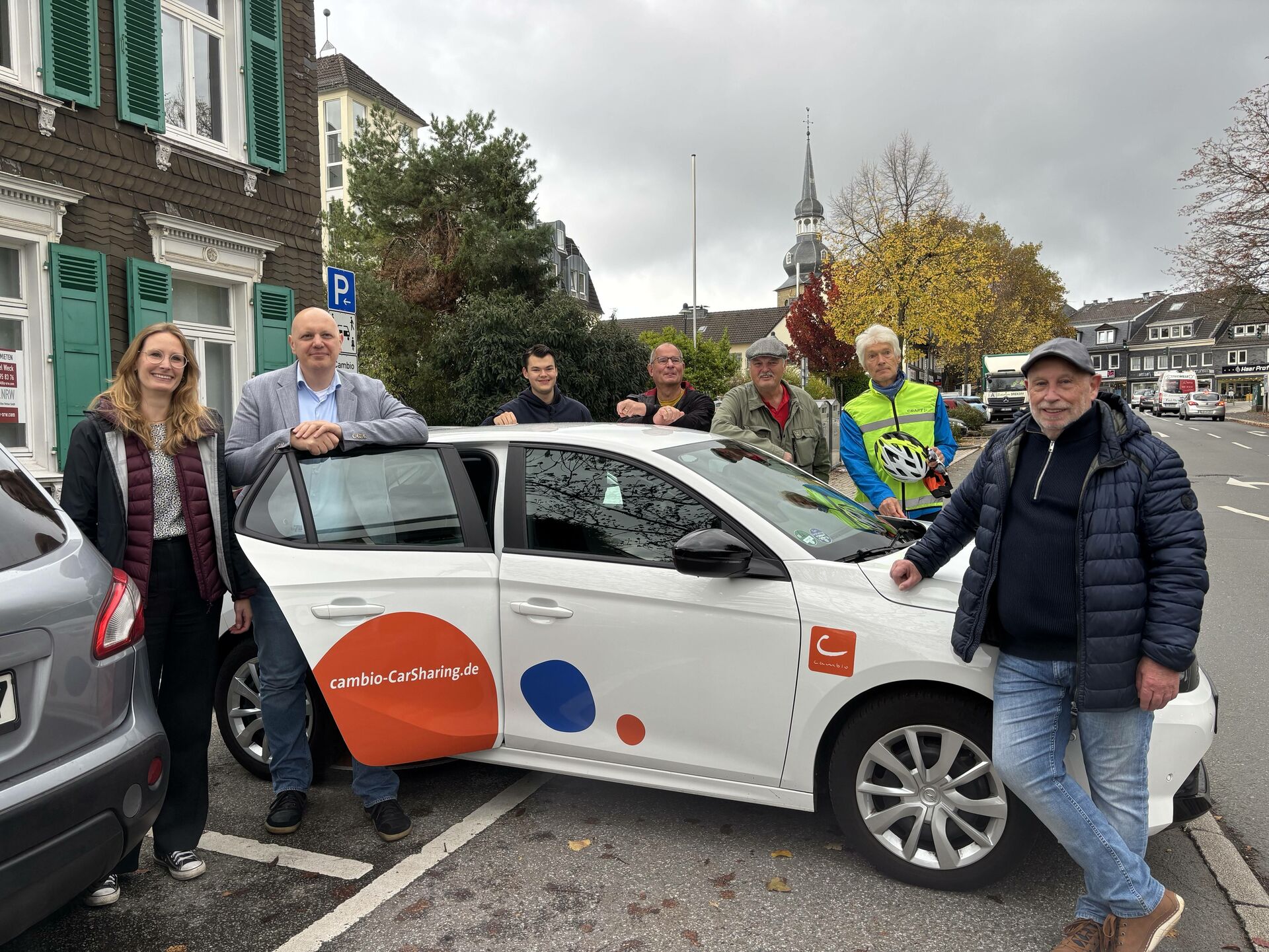 Sieben Personen stehen um ein CarSharing-Auto von cambio herum.