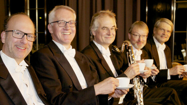 Fünf Männer in Frack lächeln in die Kamera und halten Kaffeetassen in der Hand