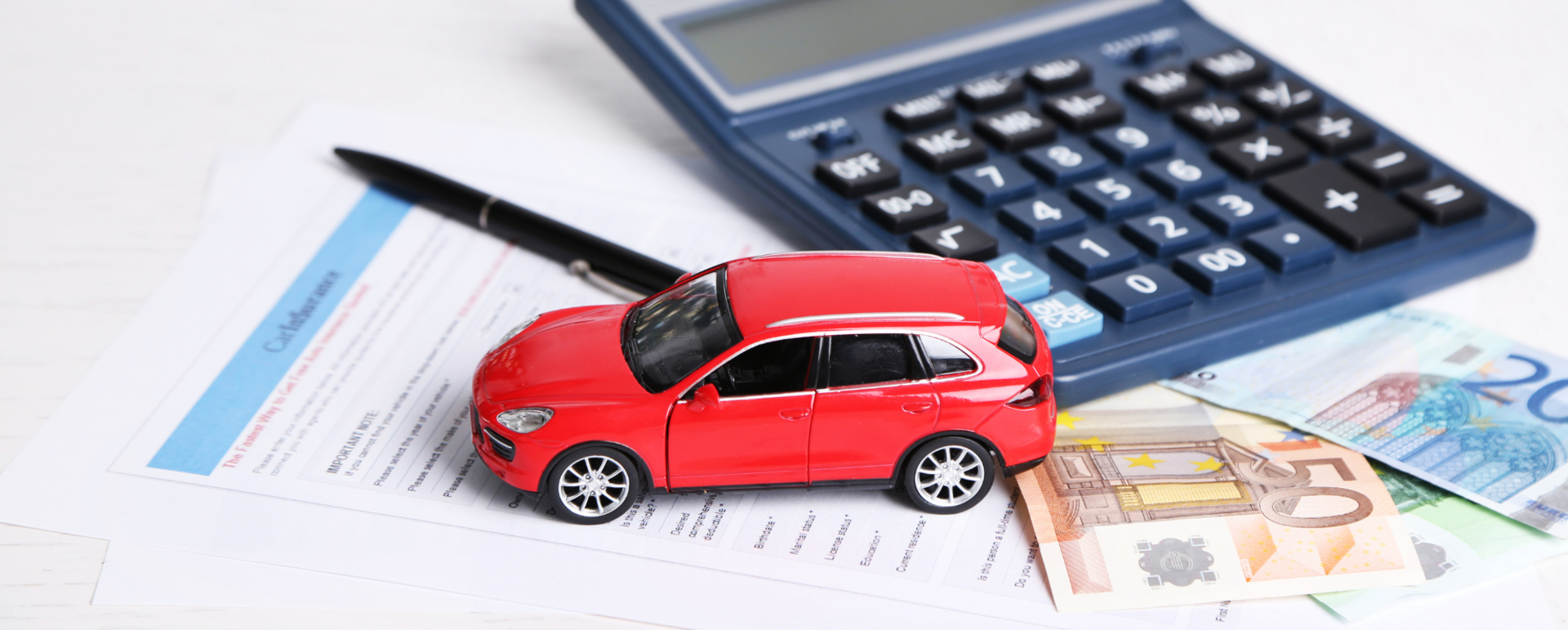 Ein Spielzeugauto vor einem Taschenrechner und Bargeld.