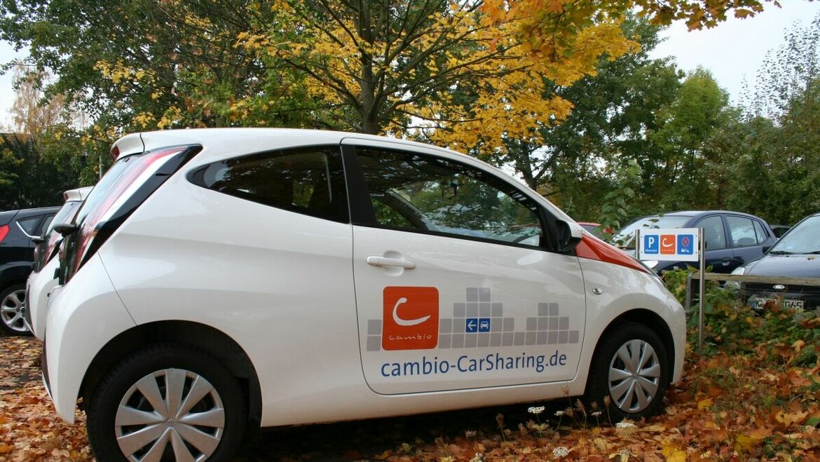 E-Auto auf einem Parkplatz von der Seite. Es liegt Herbstlaub auf dem Boden.