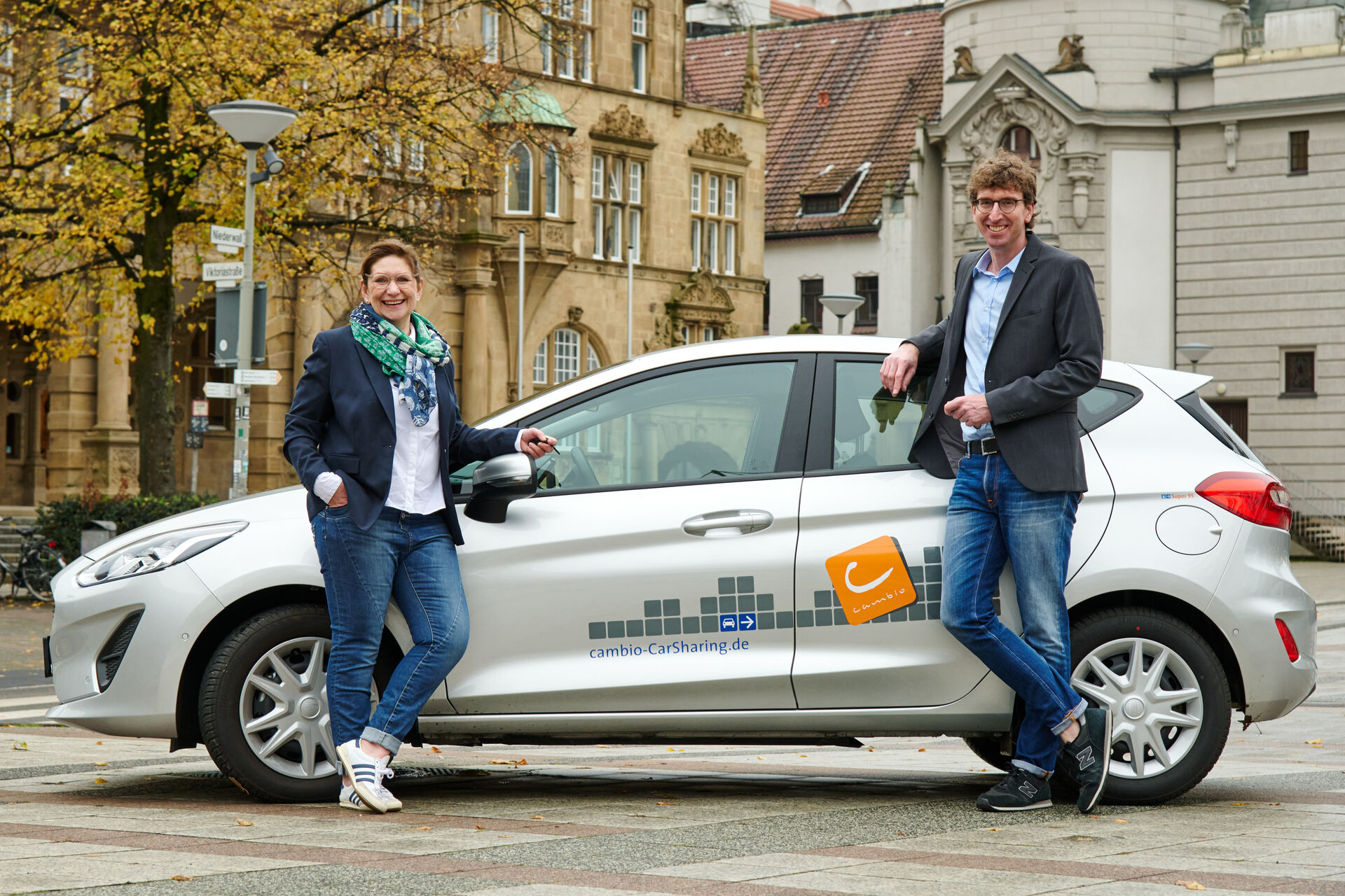 Zwei Personen, links eine Frau und rechts ein Mann, stehen vor einem cambio-Auto.