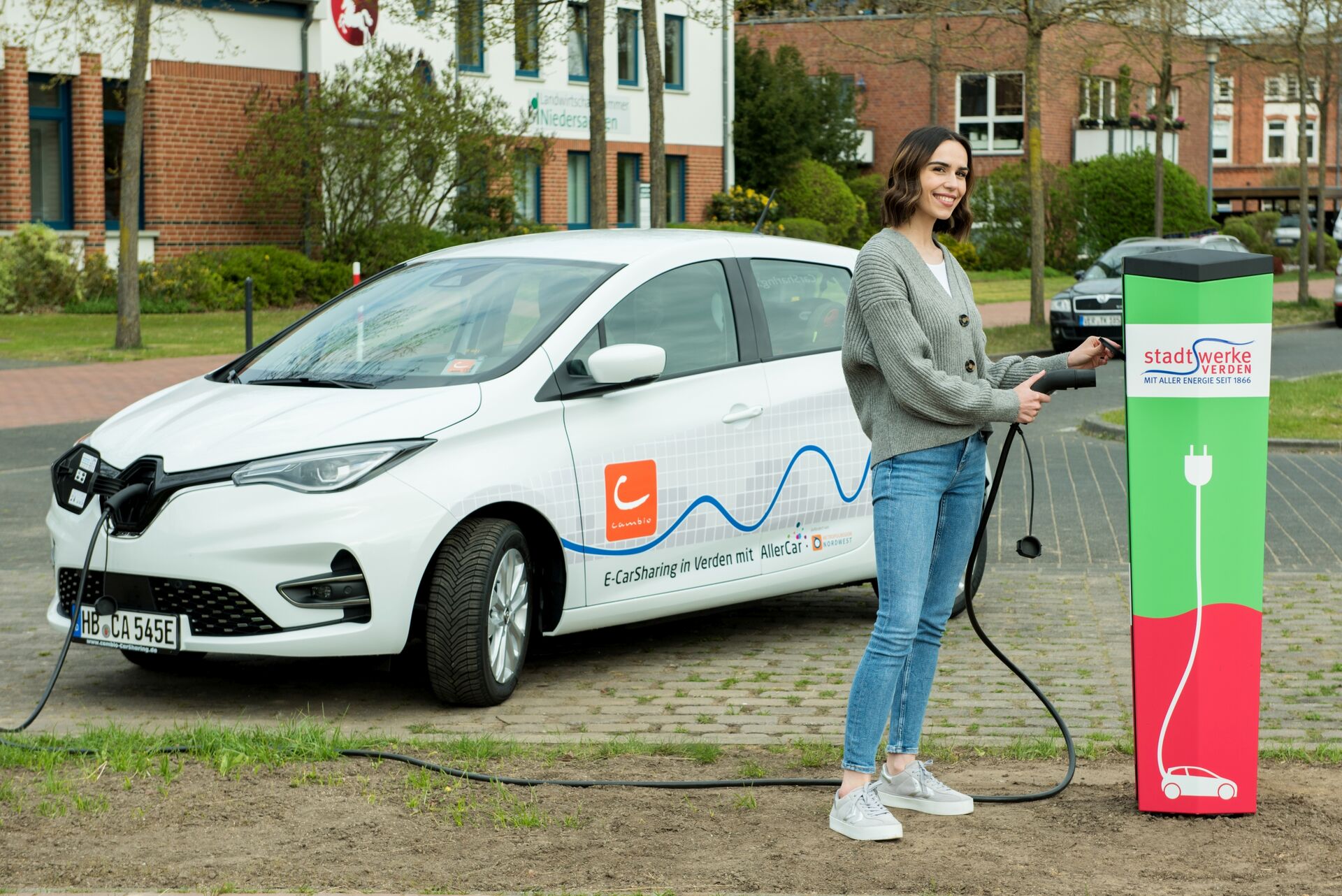 Eine Frau schließt ein weißes E-Auto an einer Ladesäule an. 