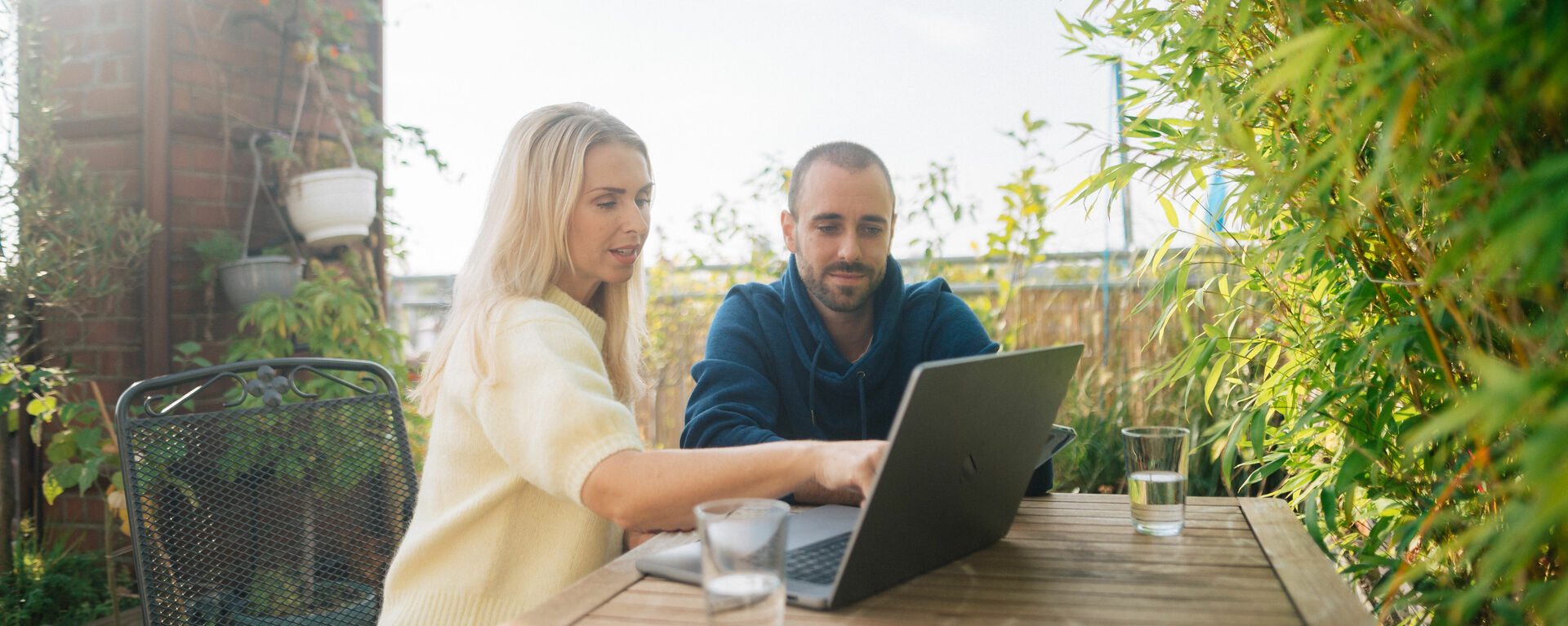In einem Garten zeigt eine Frau, einem Mann etwas an einem Laptop