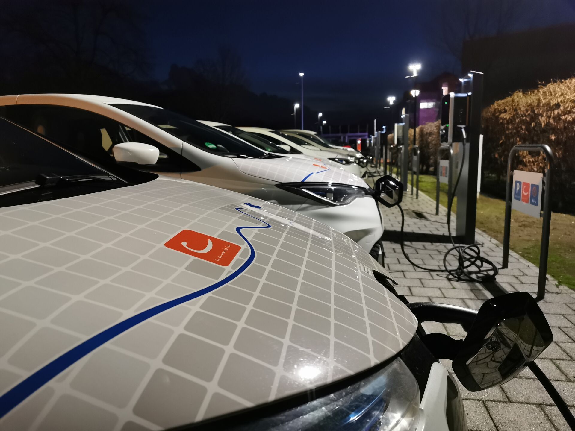 E-Autos stehen bei Nacht schräg nebeneinander und sind an Zapfsäulen angeschlossen. 