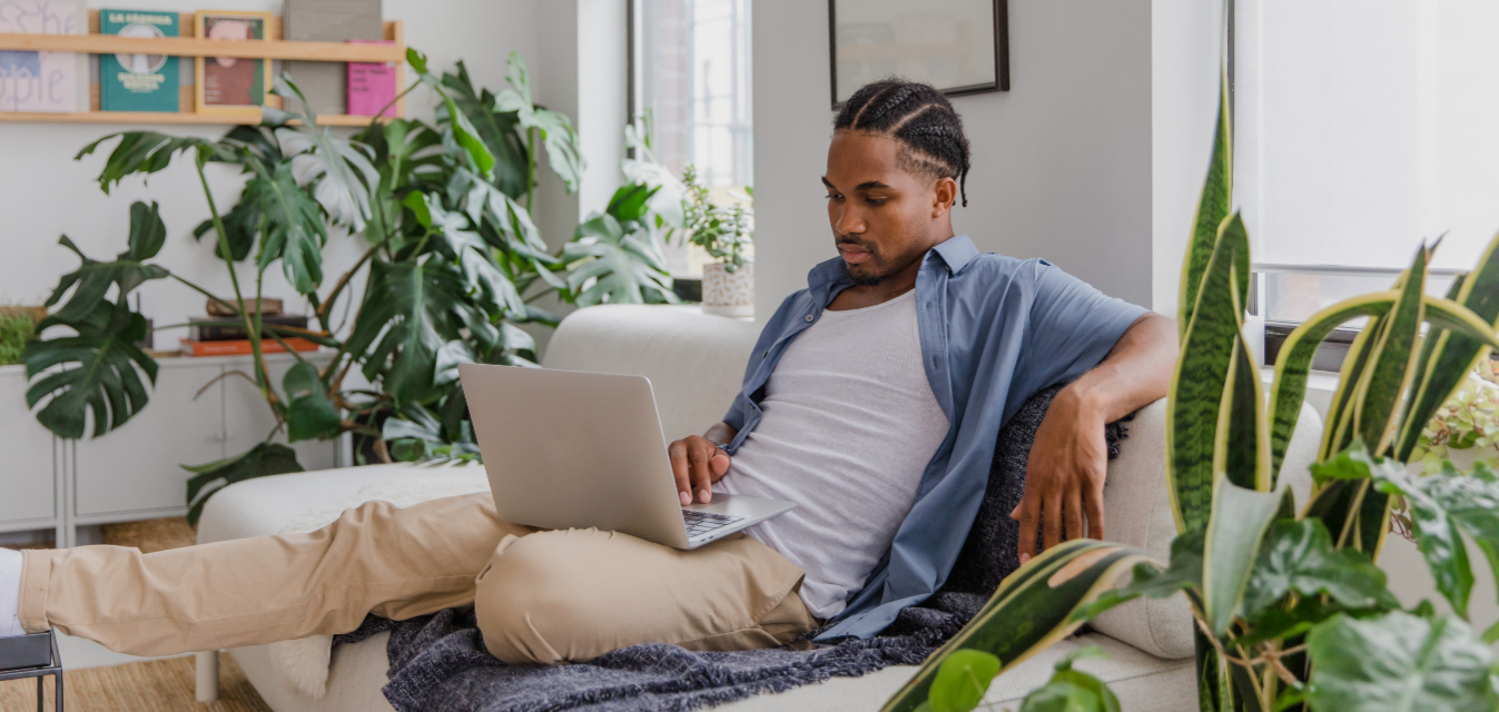 Mann sitzt auf Sofa und schaut in Laptop.