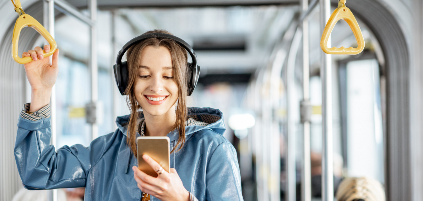 Eine Frau mit Kopfhörern fährt mit dem Bus und hält sich an einem Griff fest.