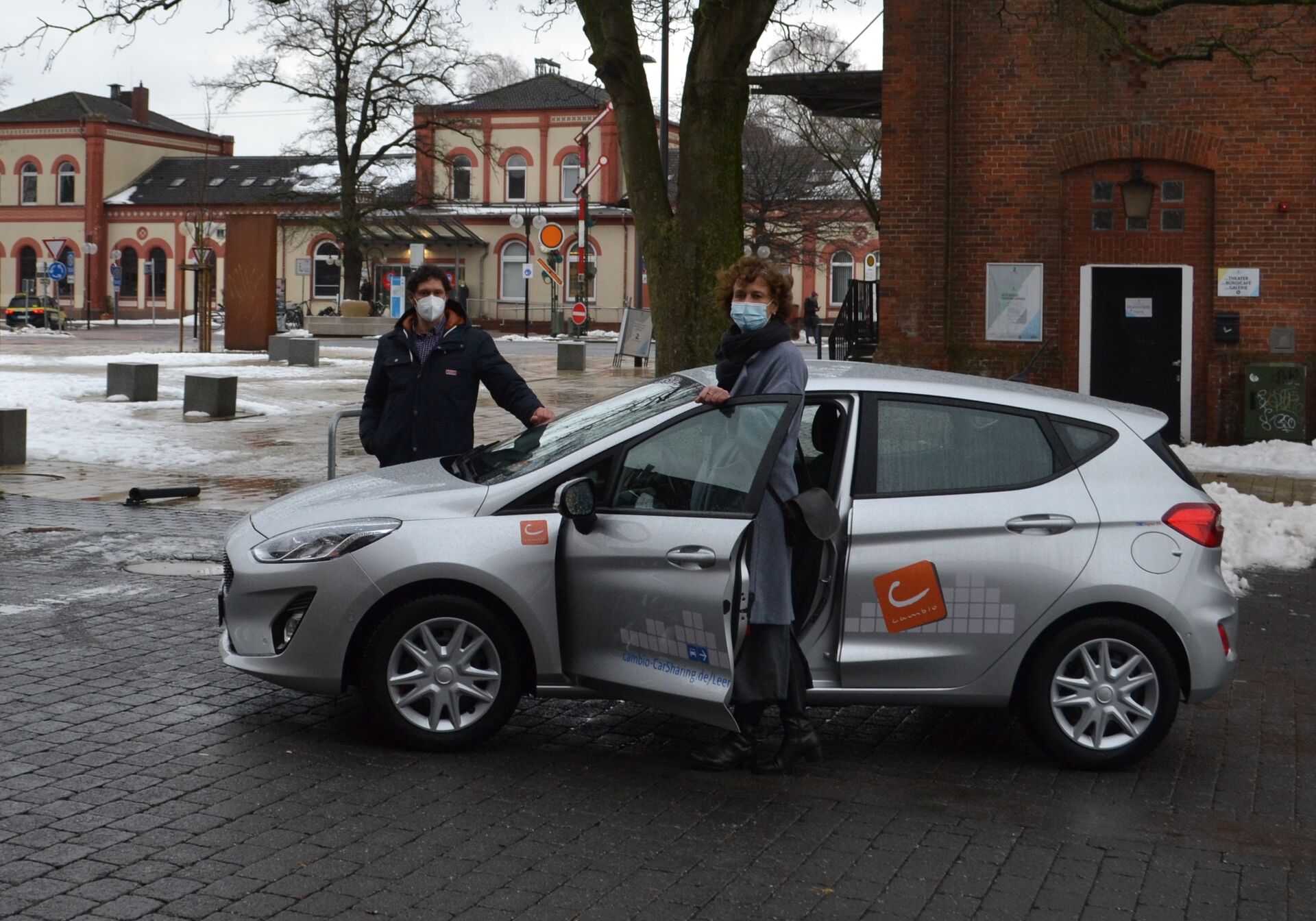 Zwei Menschen stehen an einem silbernen Auto mit Cambio Aufdruck