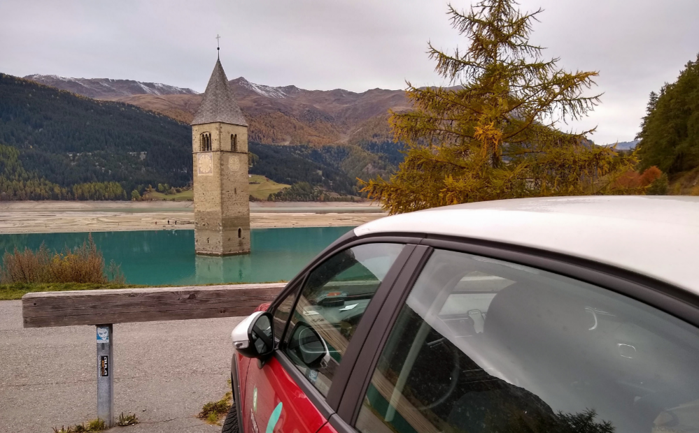 Im Vordergrund: Ein Auto. Im Hintergrund: Der Kirchturm im Reschensee