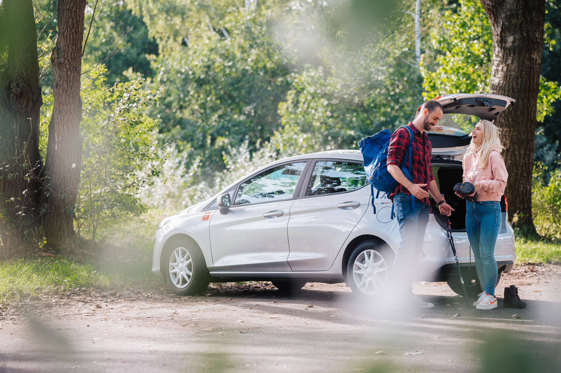 Mann und Frau am cambio-Auto bereiten sich auf Wanderung im Wald vor