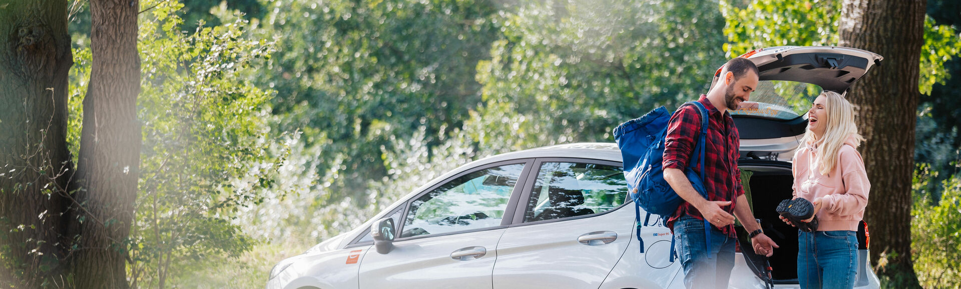 Mann und Frau am cambio-Auto bereiten sich auf Wanderung im Wald vor