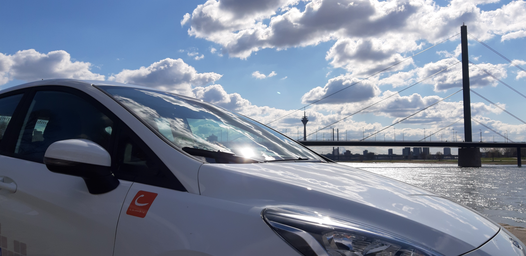 Auto im Anschnitt von der Seite, Wolken und Waser, sowie eine Brücke im Hintergrund