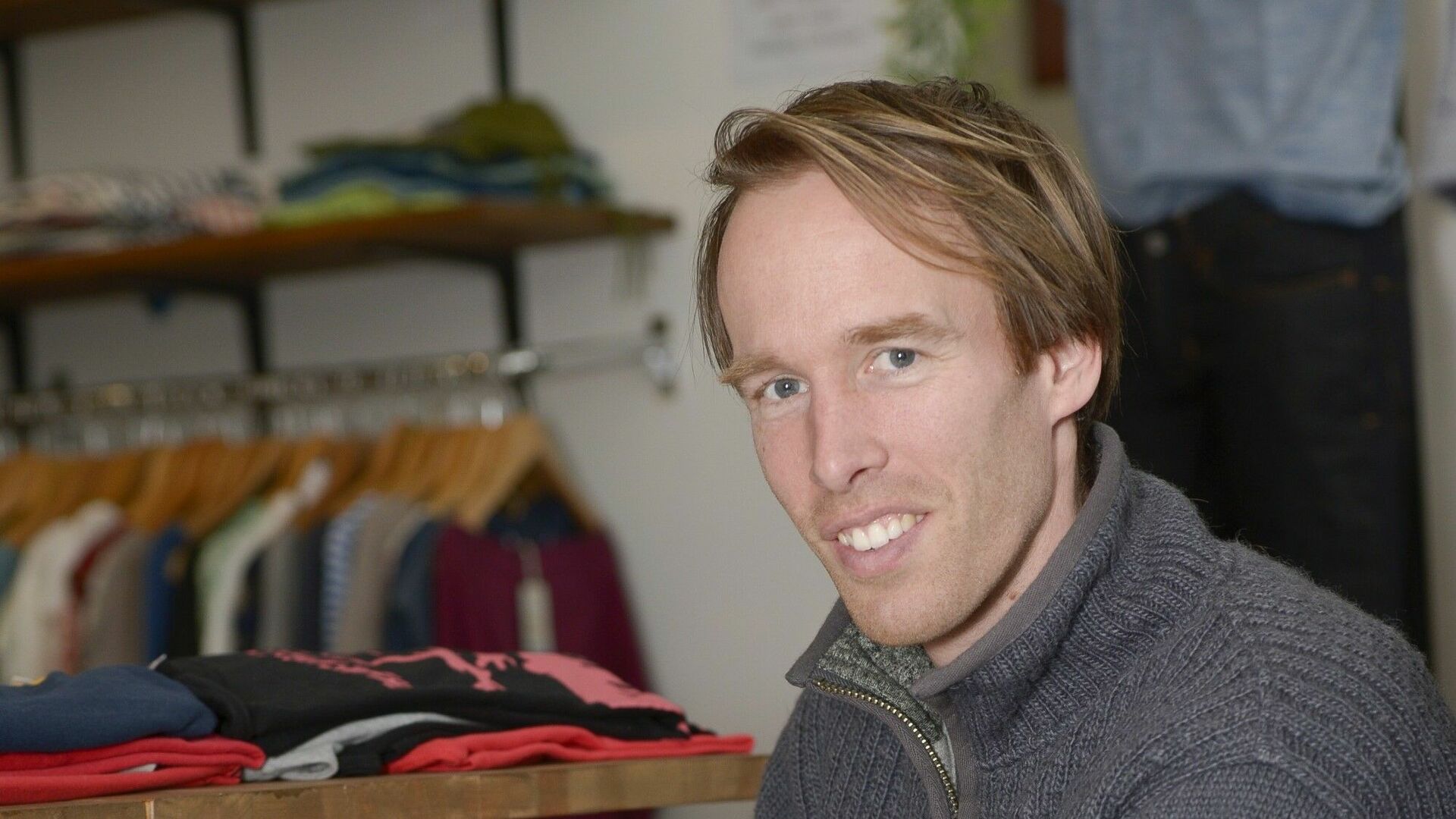 Mann in grauem Pullover lächelt in Kamera