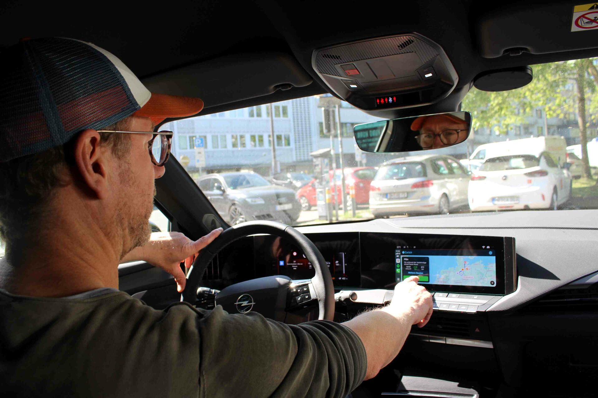 Ein Mann sitzt im Auto am Steuer und bedient das Display.