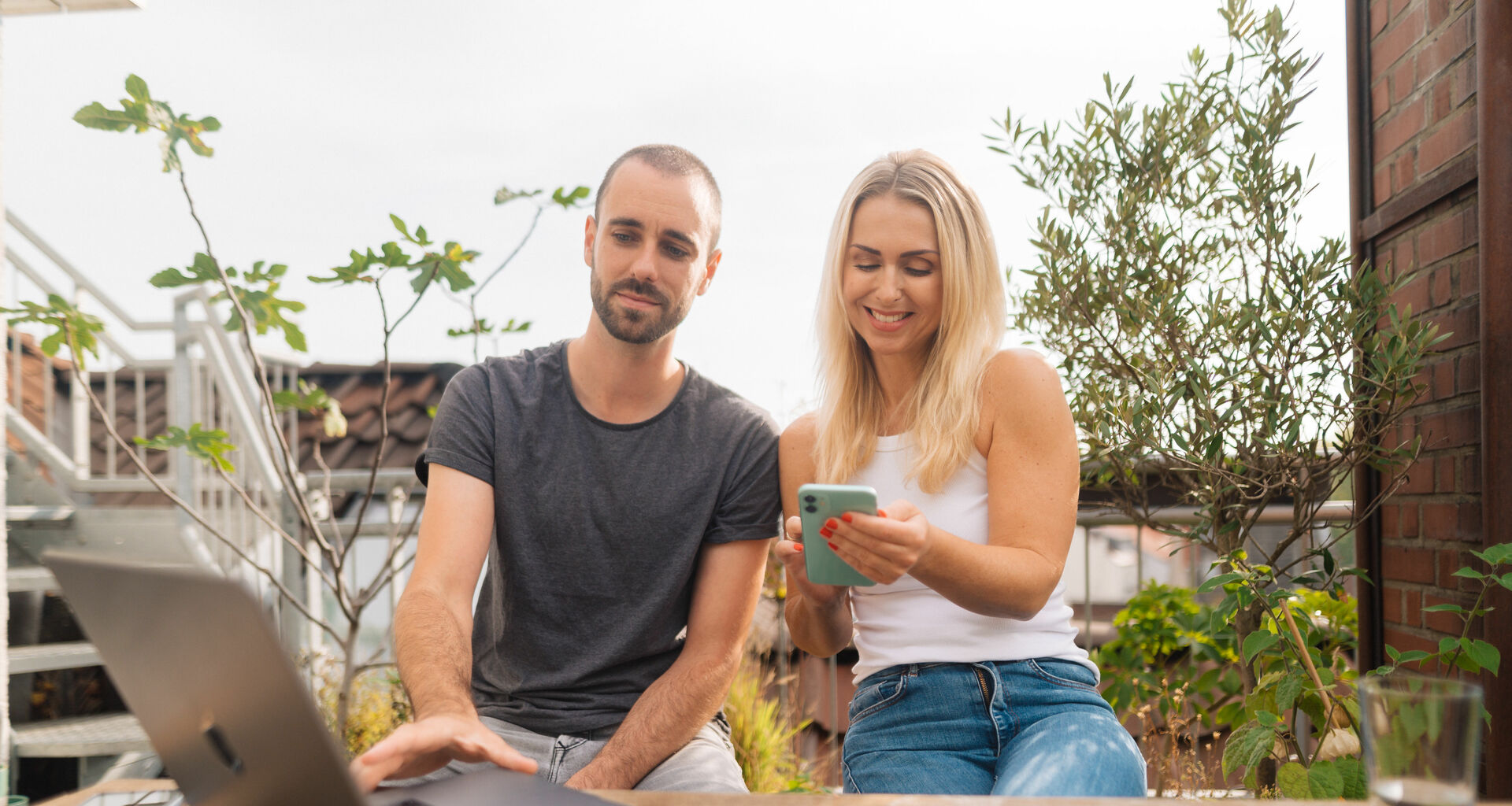 Mann und Frau schauen in ein Smartphone und haben einen Laptop vor sich
