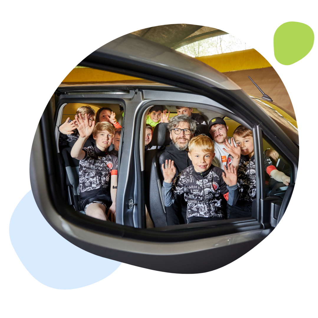 Kinder sitzen mit zwei Erwachsenen in einem Fahrzeug und winken in die Kamera.