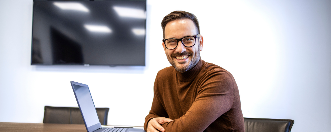 Mann vor Laptop schaut freundlich in die Kamera