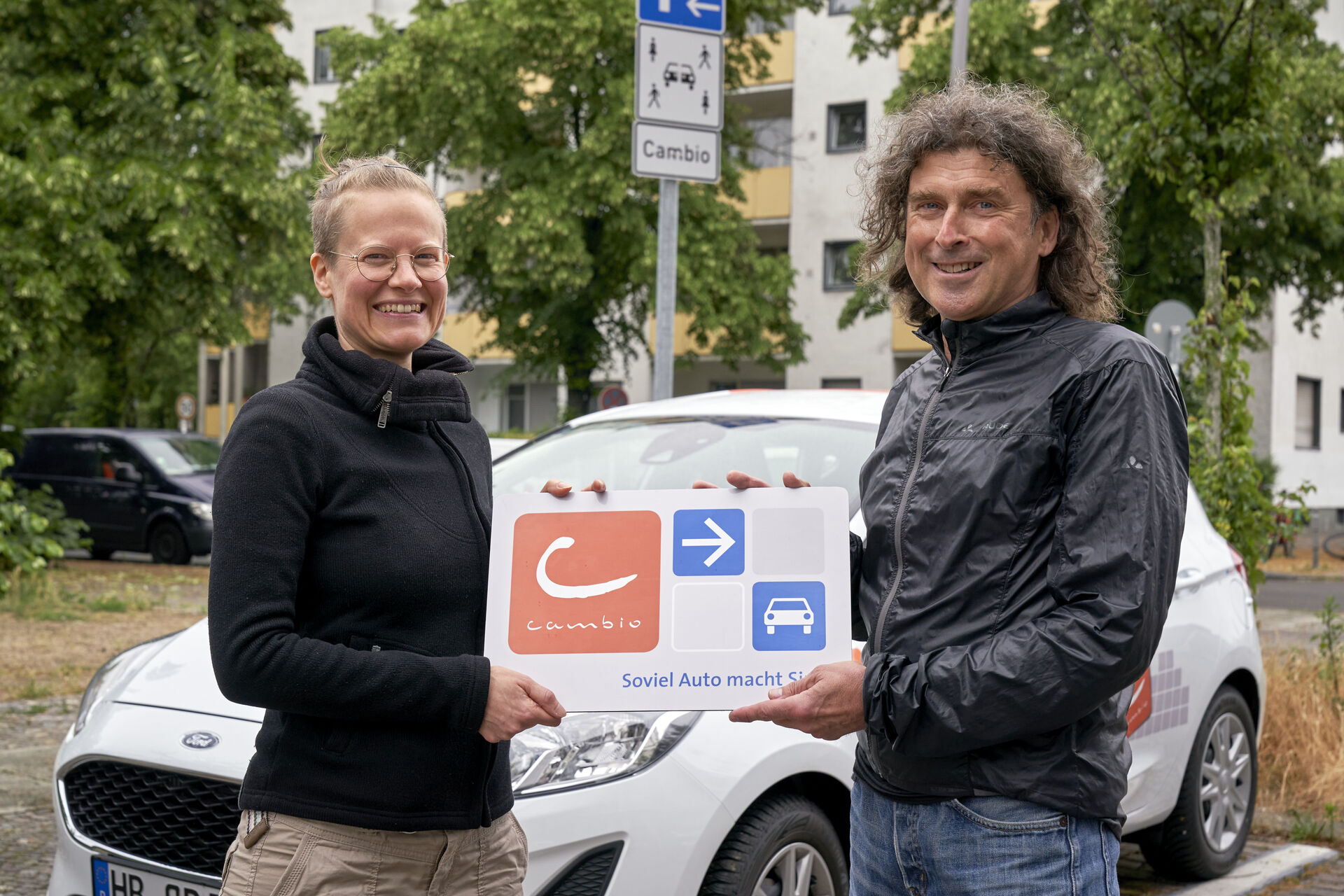 Bild von Helmut Gerlach und Alexandra Lermen vor einem Cambio-Auto, beide halten ein Schild mit dem Cambio-Logo