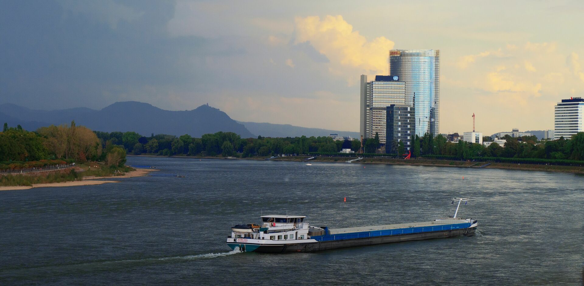 Binnenschiff fährt auf einem Fluss, im Hintergrund sieht man hohe Gebäude