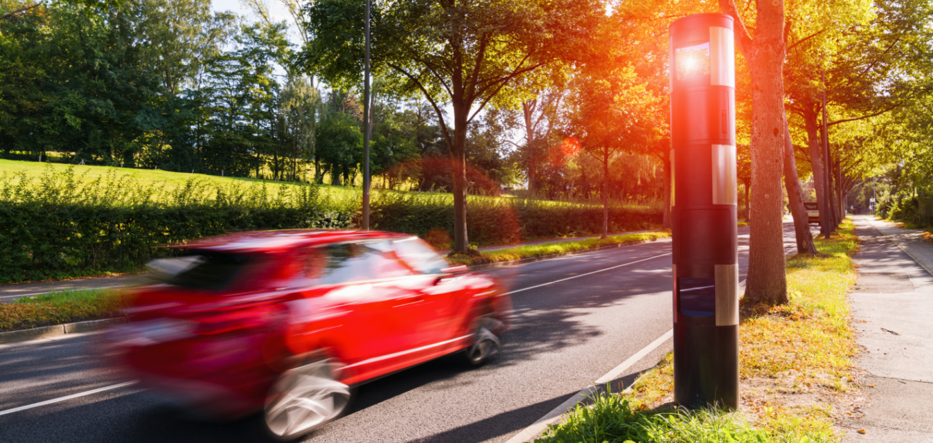 Ein rotes Auto wird von einer elektronischen Geschwindigkeitskontrolle geblitzt