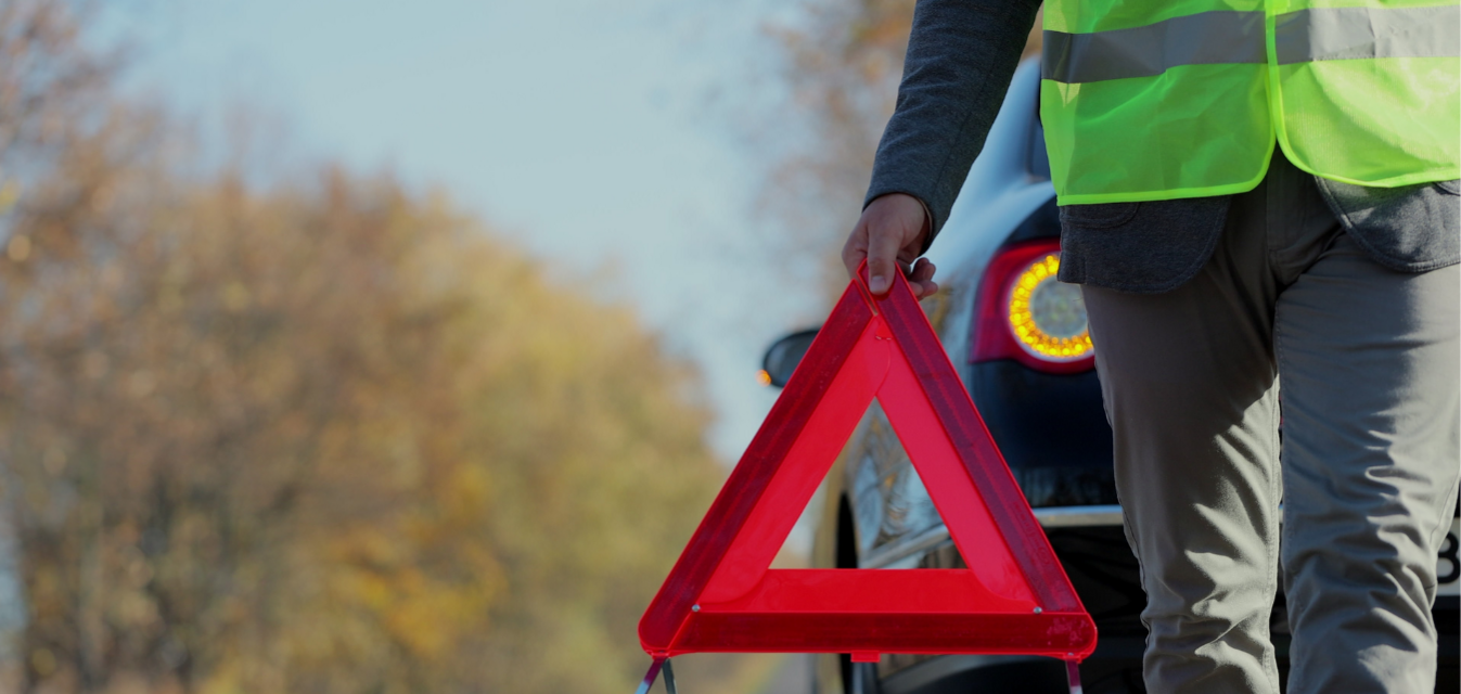 Person mit gelber Weste stellt Warndreieck auf