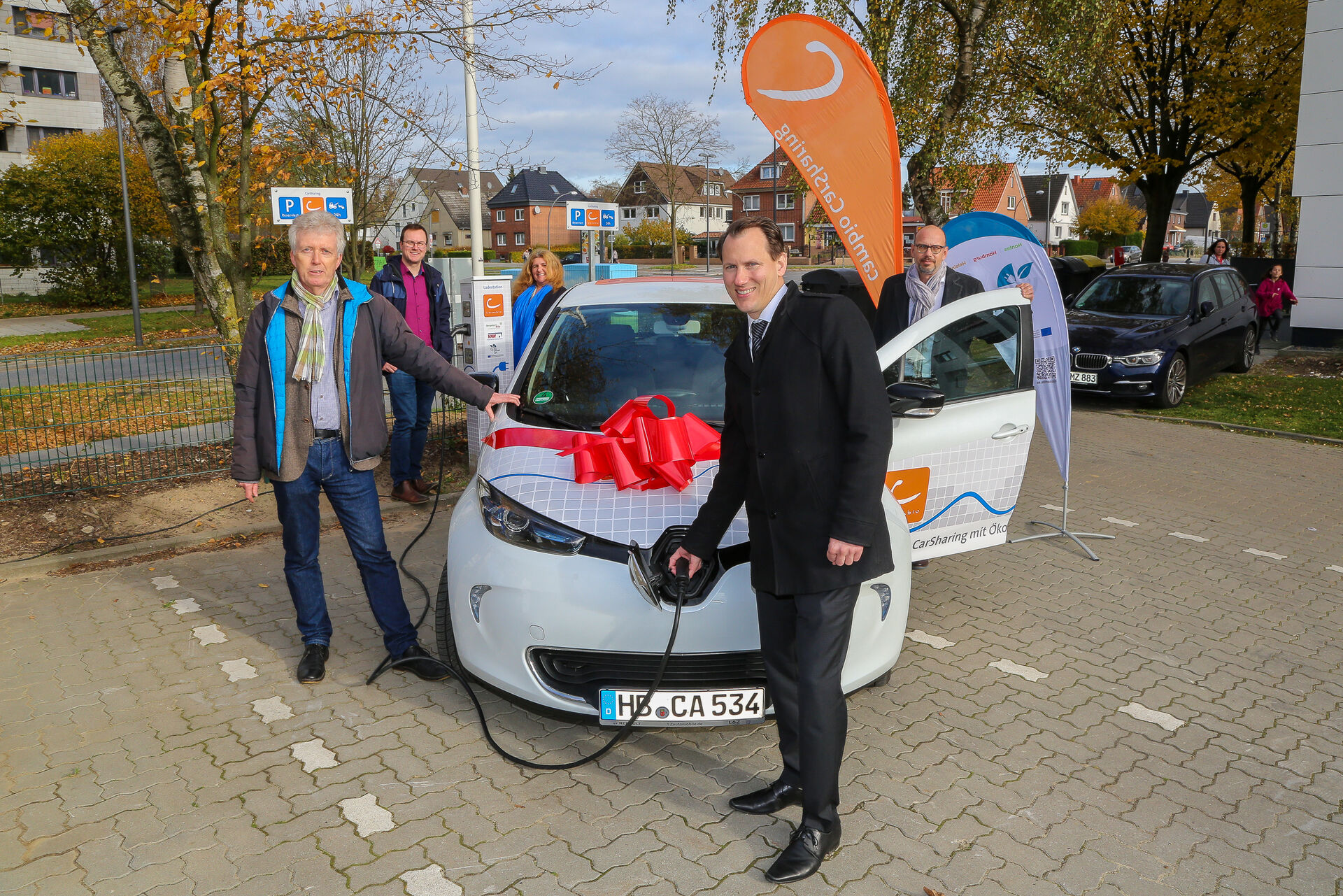 Ein Mann lädt ein cambio-Auto auf, das eine Geschenkschleife auf der Motorhaube hat