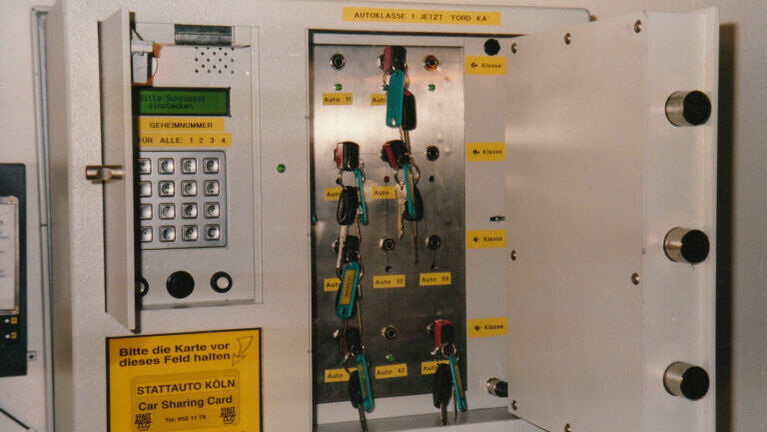 Elektronischer Tresor. Links ein Pinpad für den Code zum Öffnen. Rechts die geöffnete Tür, es hängen mehrere Autoschlüssel in Nummern darin.