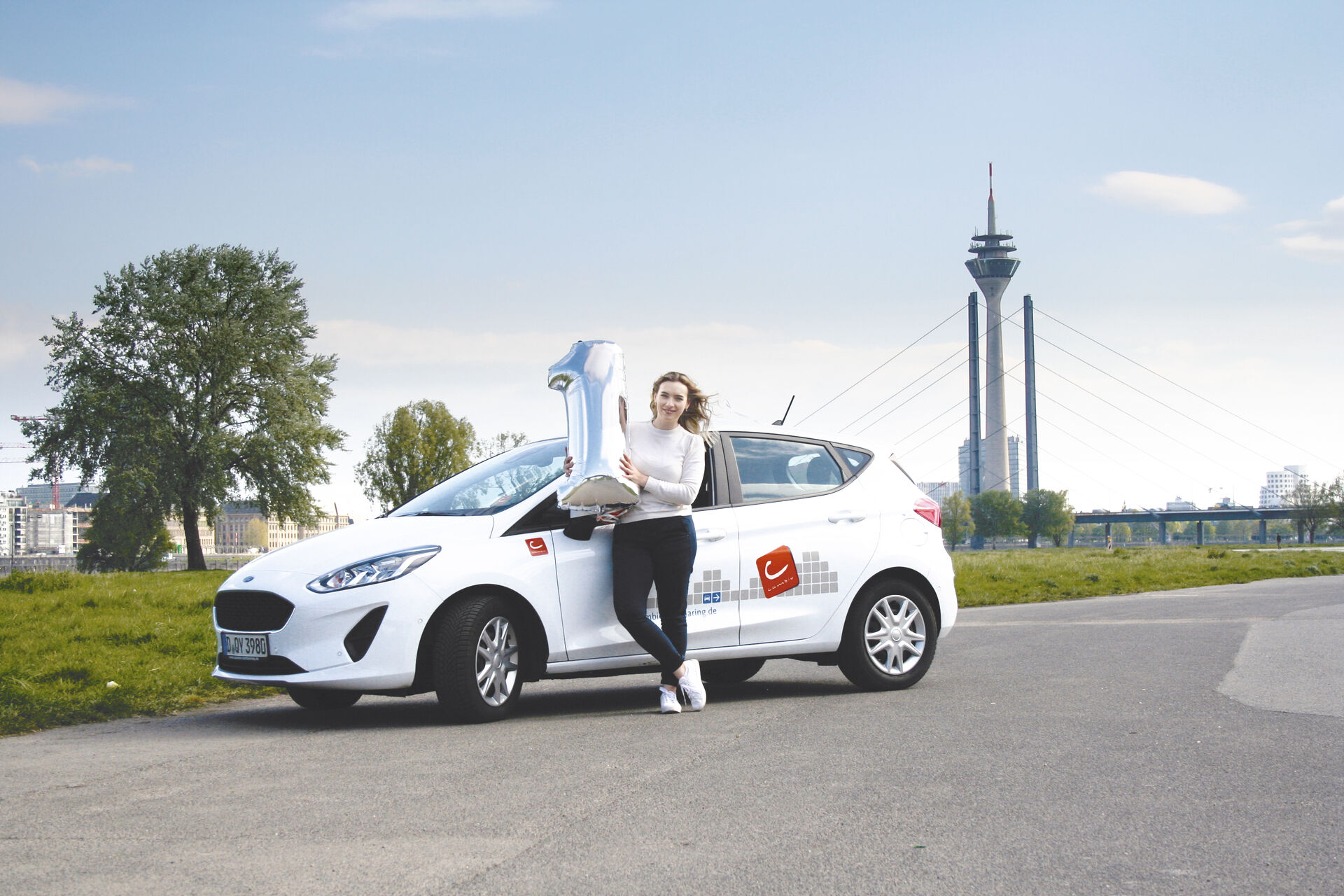 Frau steht mit einer Ballon Eins vor einem weißen E-Auto