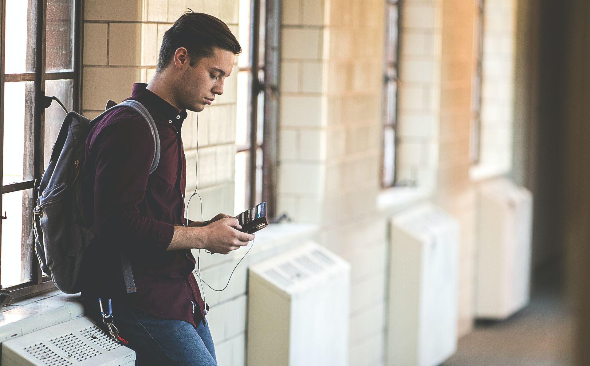 Ein junger Mann steht an einer Wand und guckt auf ein Smartphone