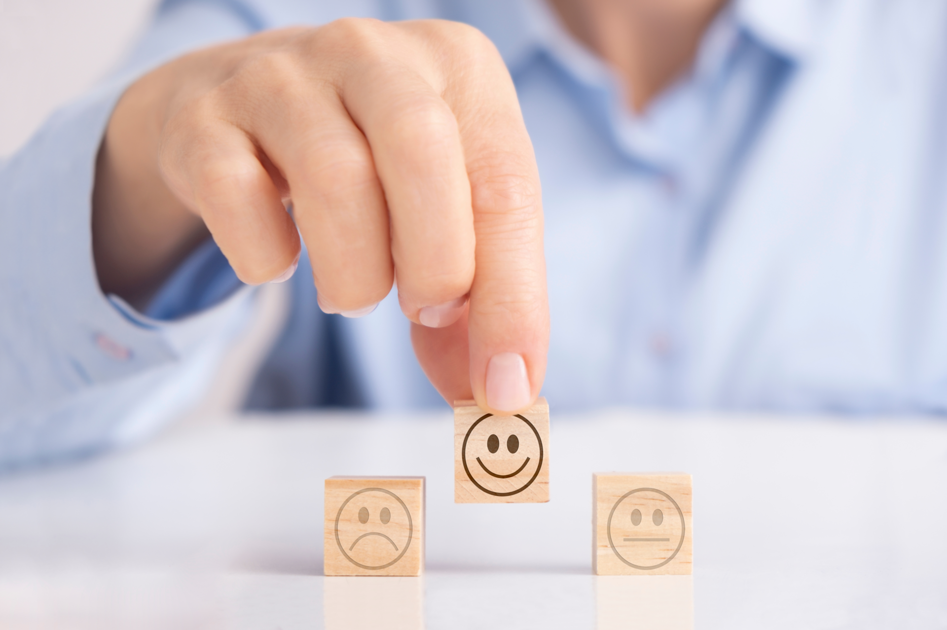 Drei Holzwürfel mit Emoji: Freude, neutral, Trauer