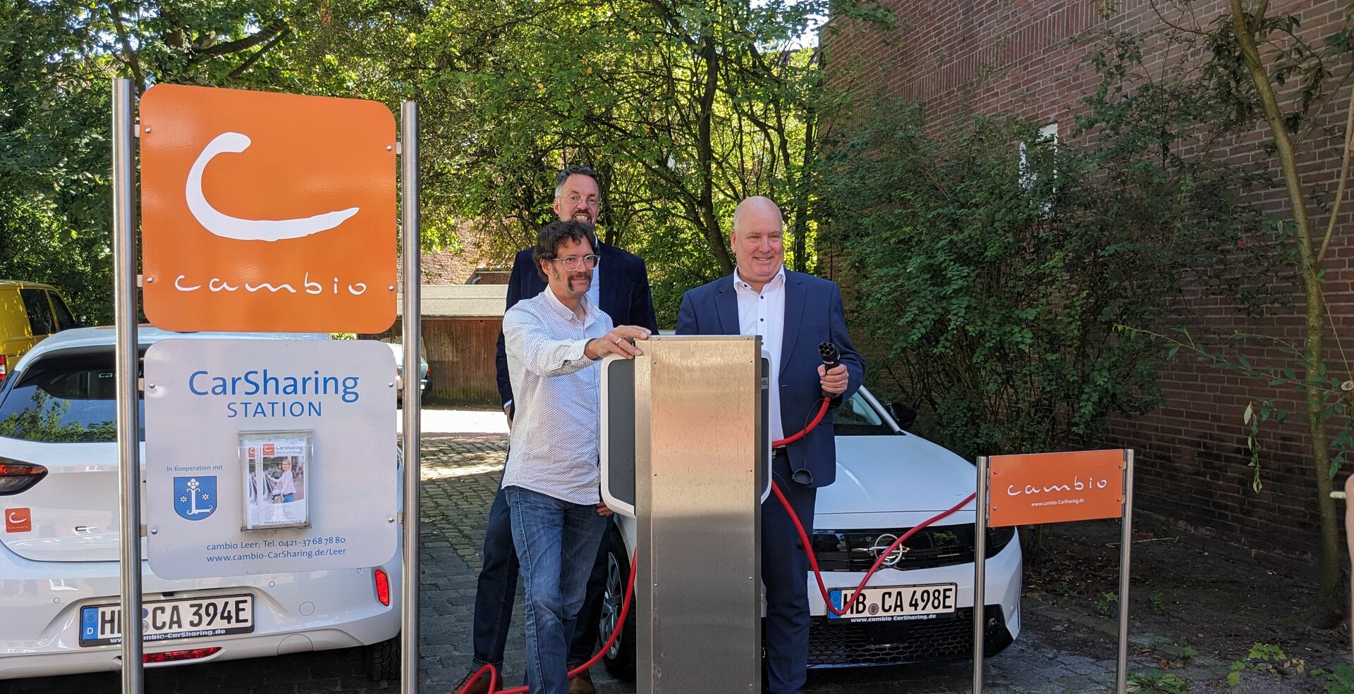 Drei Personen stehen an einer Ladesäule und lächeln in die Kamera