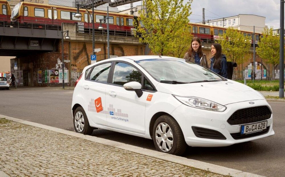 Zwei Frauen stehen am cambio-Auto. Im Hintergrund eine Überführung der Berliner S-Bahn