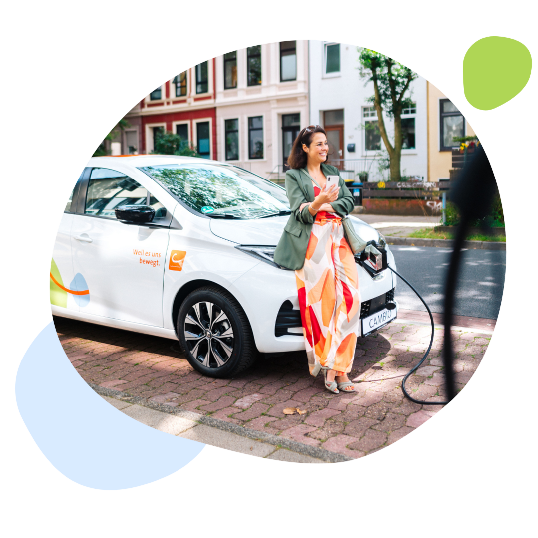 Eine Frau steht mit dem Smartphone an der Hand an einem E-Auto von cambio. Im Hintergrund ist eine Straße und Häuser zu sehen.