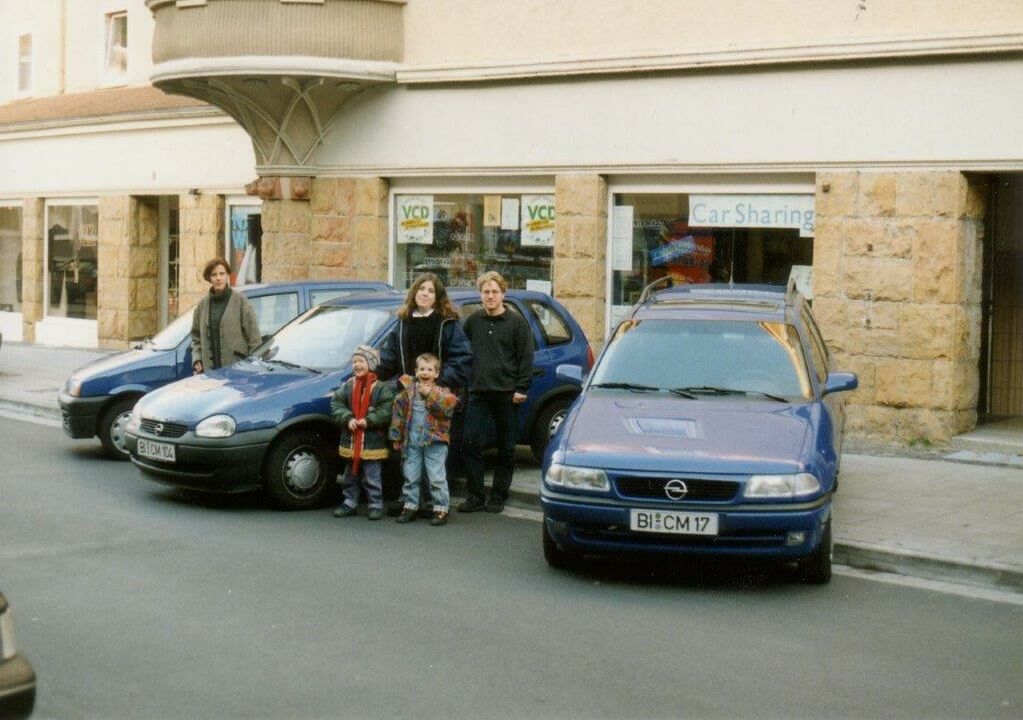 Drei Opel Corsa stehen nebeneinander auf der Straße mit der Front zur Kamera. Daneben fünf Personen. Das Foto ist Anfang 2000 entstanden.