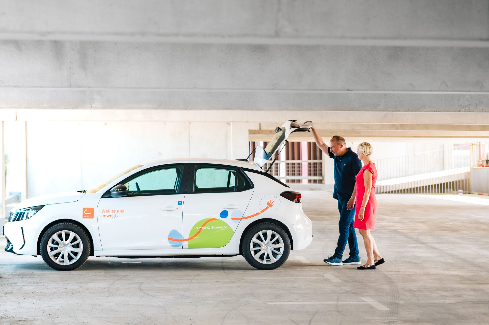 Zwei Personen stehen in der Tiefgarage am geöffneten Kofferraum eines CarSharing-Autos.