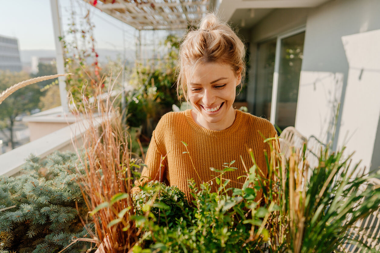 Eine Frau steht lächelnd auf ihrem Balkon und schaut auf einen Kräutergarten